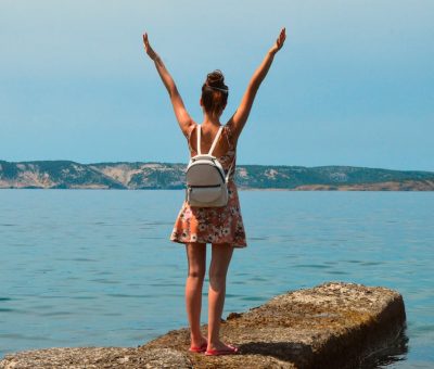 Woman in floral dress with arms raised, enjoying the view by the sea in Croatia.